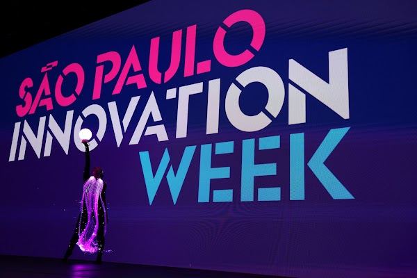 Bailarina com figurino de luz diante do painel São Paulo Innovation Week na abertura